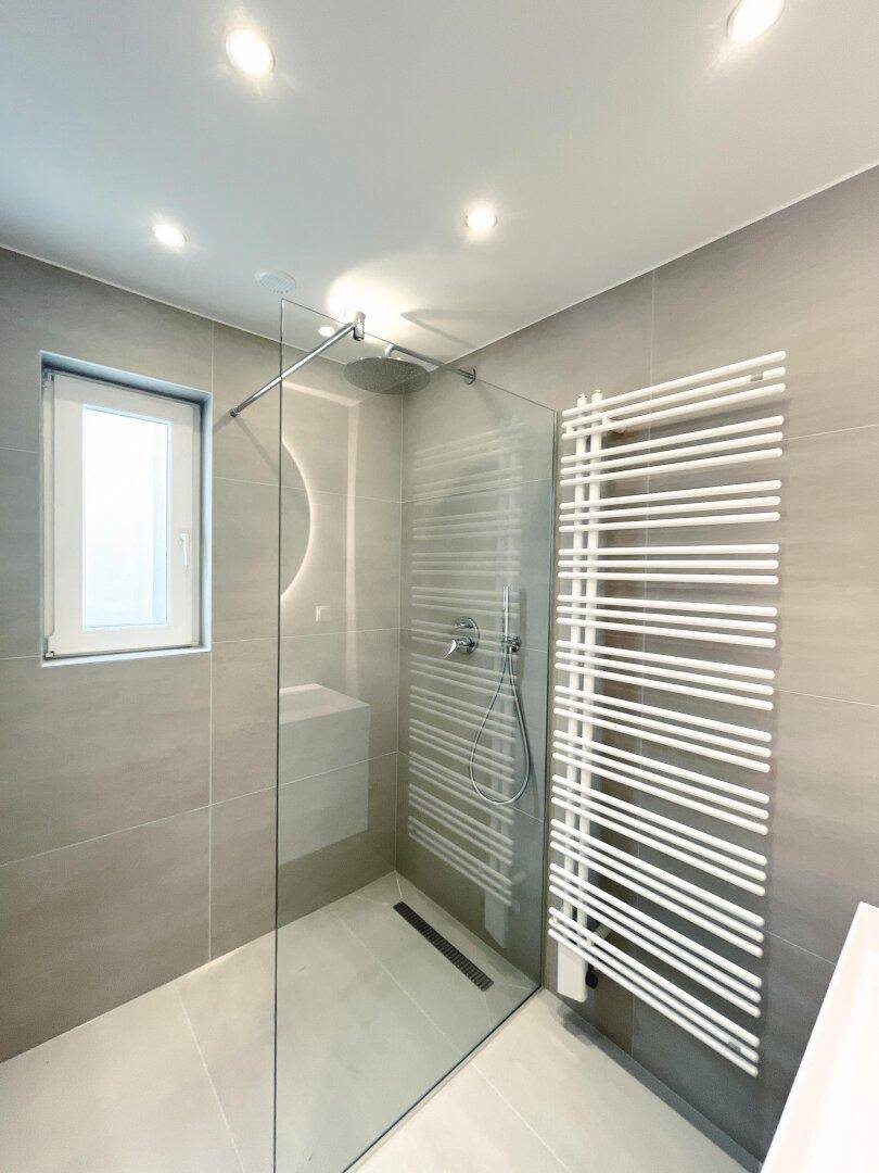 Modernes Badezimmer mit grauen Fliesen, begehbarer Dusche und beheiztem Handtuchhalter.