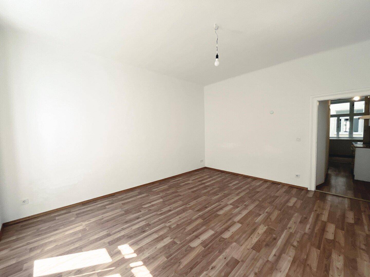 Geräumiger, heller Raum mit Laminatboden und Zugang zu einem weiteren Zimmer.