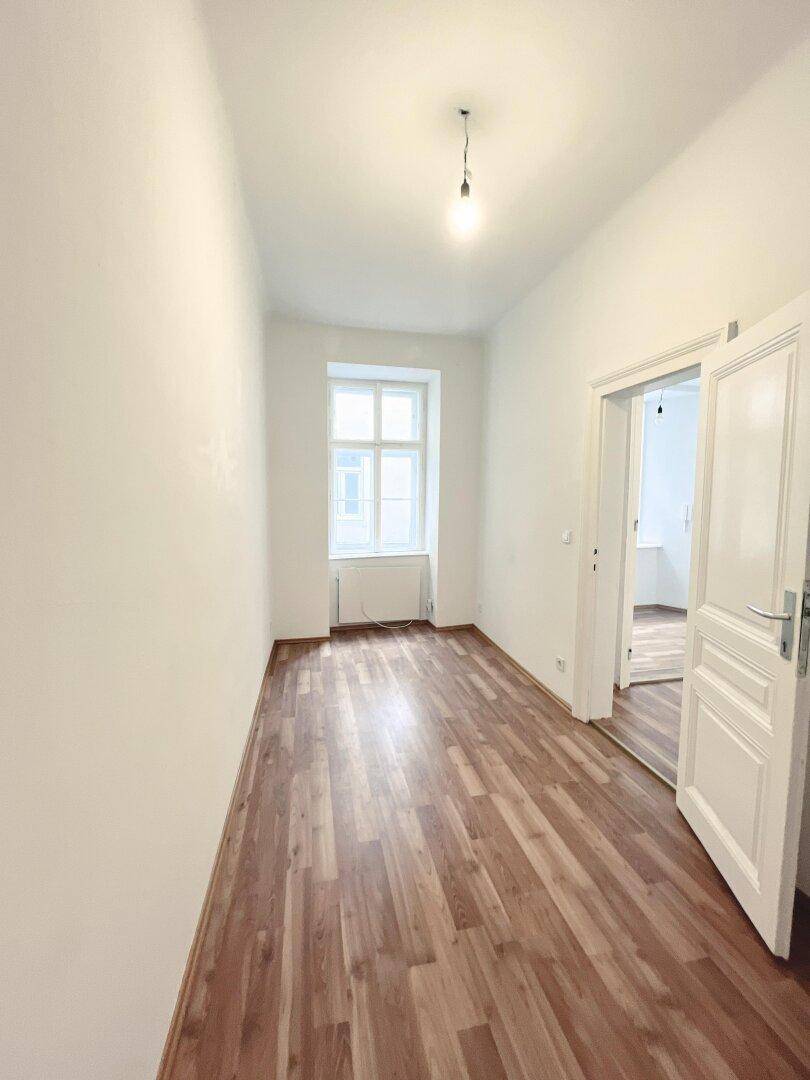 Schmaler, heller Flur mit Laminatboden und Fenster, der zu weiteren Räumen führt.
