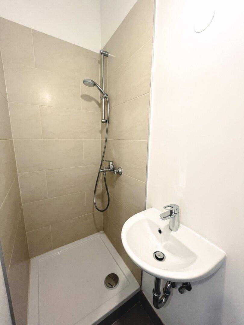 Modernes Badezimmer mit Duschbereich und kleinem Waschbecken, hell gefliest.