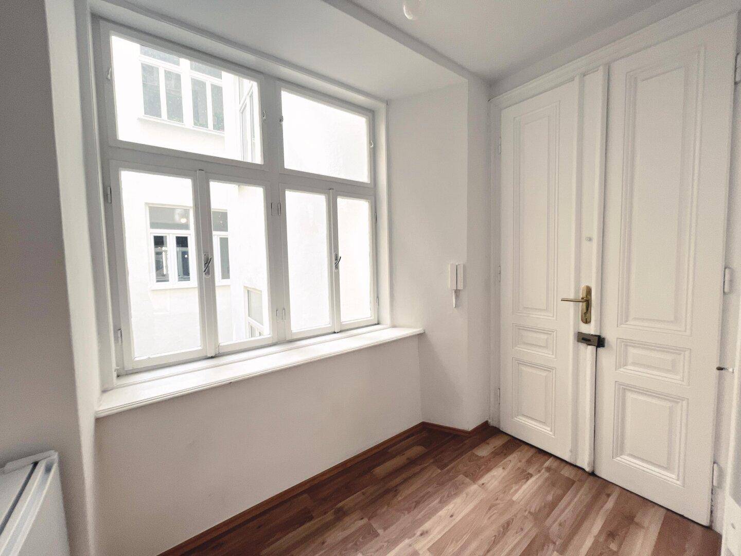 Heller Eingangsbereich mit großem Fenster und klassischen Doppeltüren.