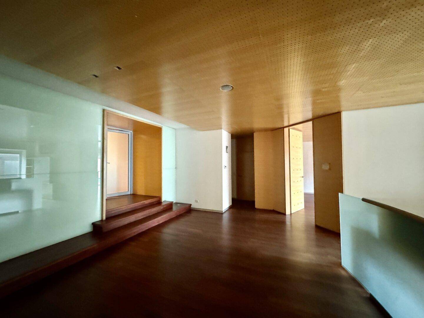 Raum mit Holzboden, einer erhöhten Plattform mit Stufen und eleganten Holzvertäfelungen an den Wänden.