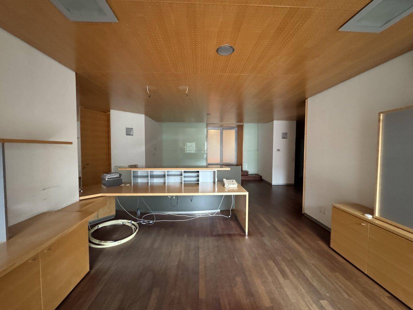Büroraum mit Holzboden, perforierter Holzdecke und mehreren Schreibtischen sowie Schränken.