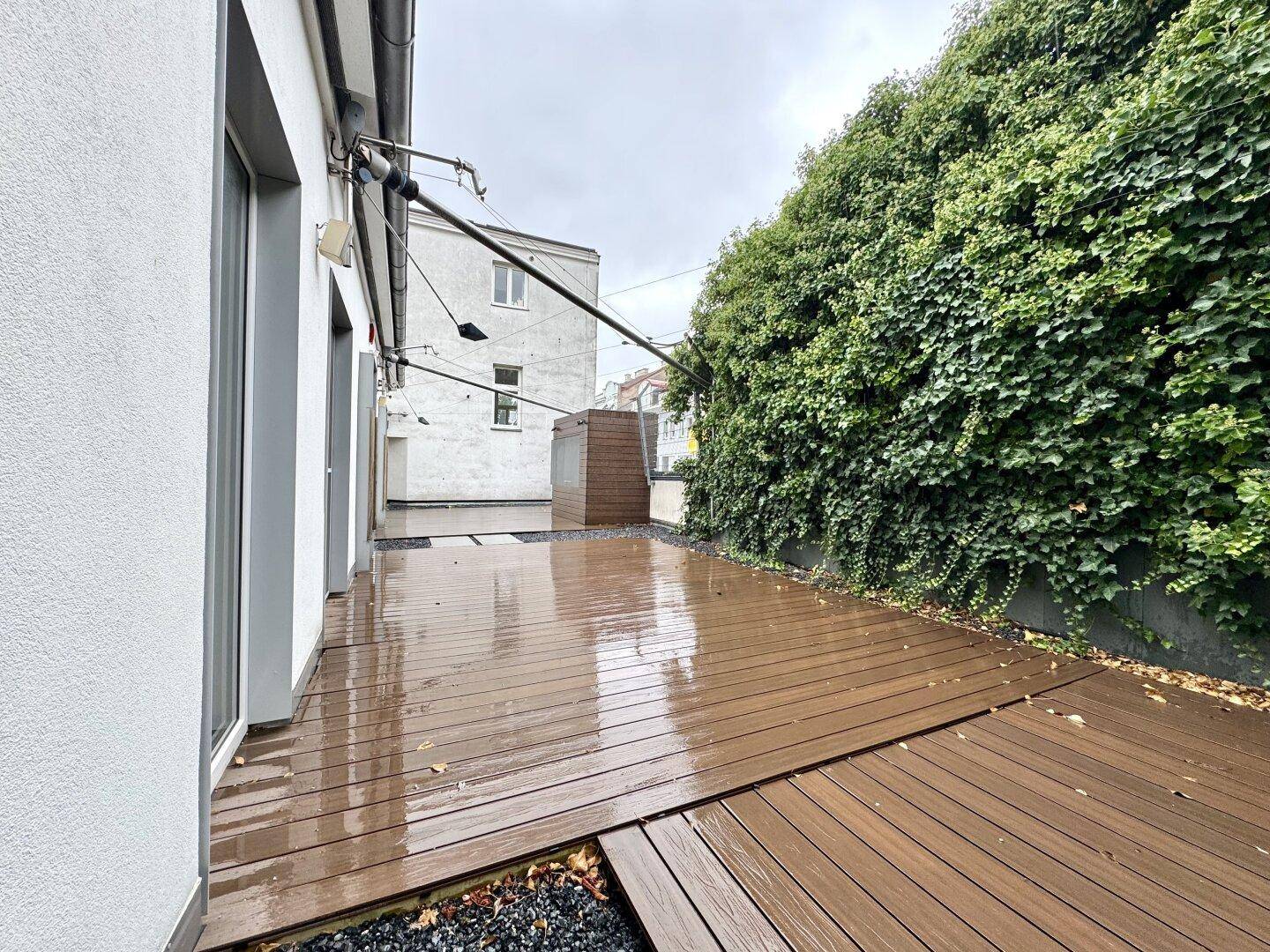 Weitläufige Terrasse mit Holzdielen und einer hohen, mit Efeu bewachsenen Wand, die eine natürliche Abgrenzung bildet.