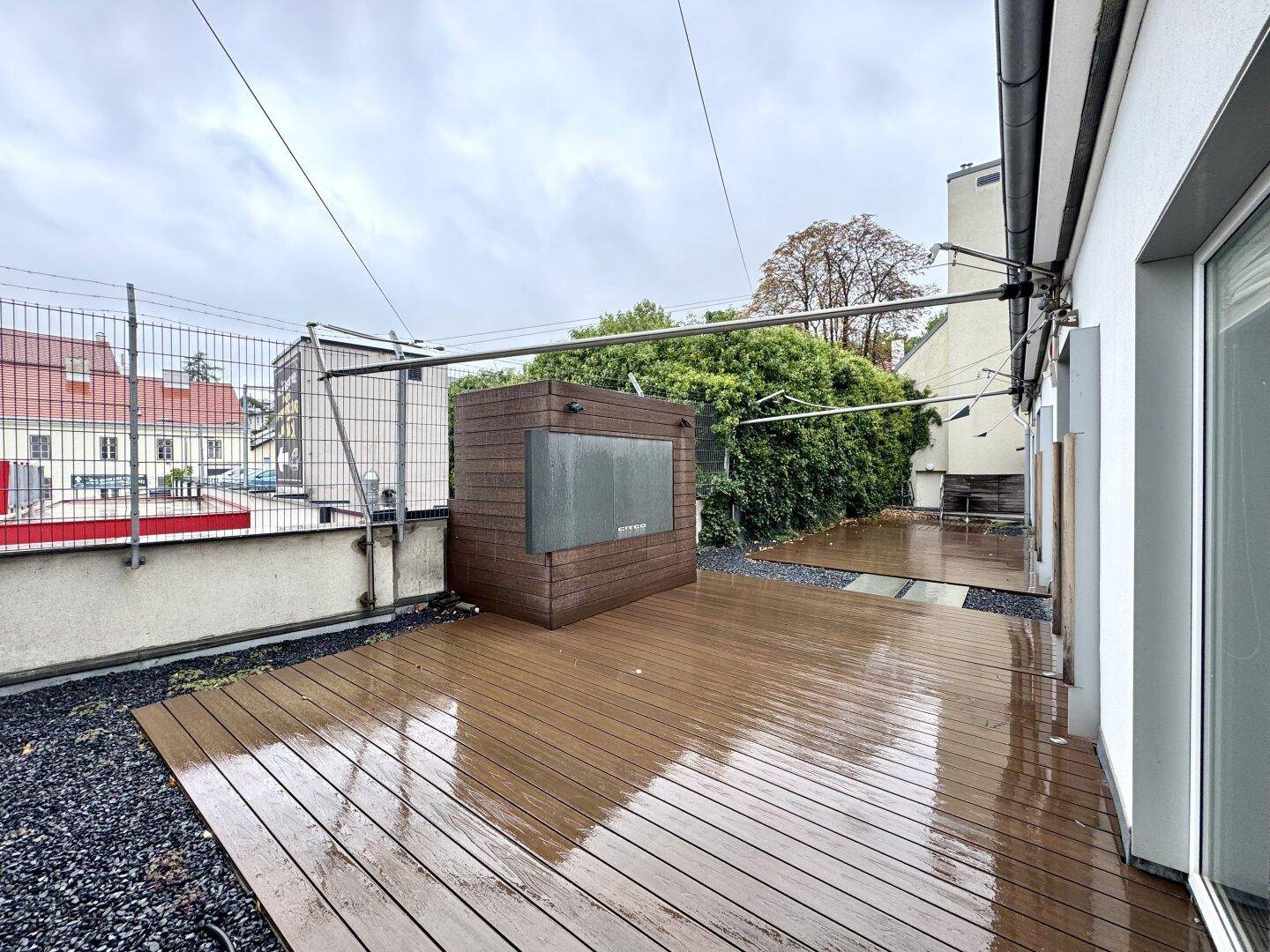 Eine geräumige Außenterrasse mit Holzdielenboden, dunklem Kies und einer modernen Holzstruktur unter bewölktem Himmel.