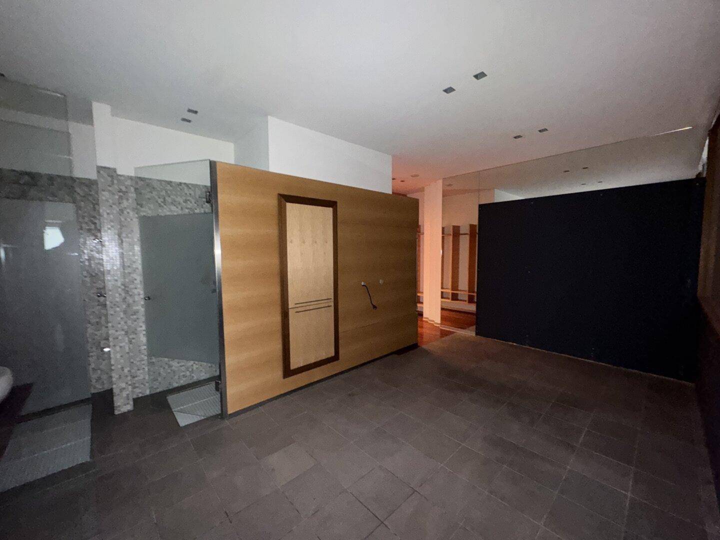 Badezimmer oder Umkleidebereich mit dunklem Fliesenboden, einer Duschkabine und einer Holztür, die an eine Sauna erinnert.