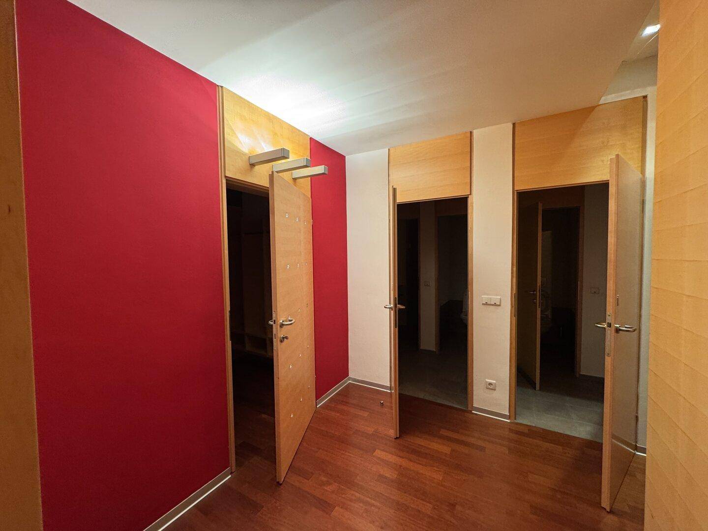 Flur mit Holzboden, einer lebhaften roten Akzentwand und mehreren Holztüren, die zu verschiedenen Räumen führen.