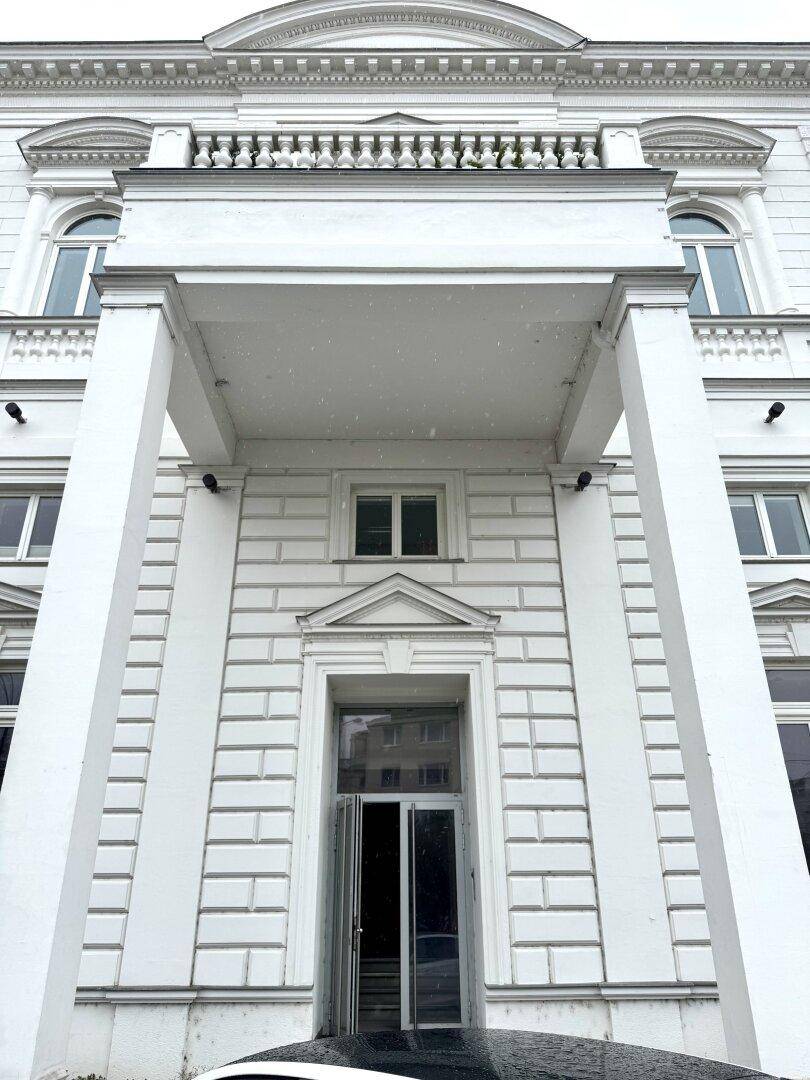 Klassische weiße Fassade eines Gebäudes mit Säulen, Balkon und großen Fenstern.
