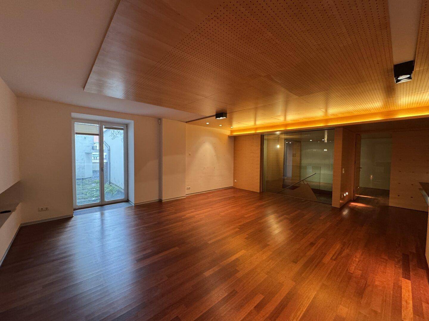 Heller Wohnraum mit Holzboden, perforierter Holzdecke und großer Glasschiebetür zum Außenbereich.