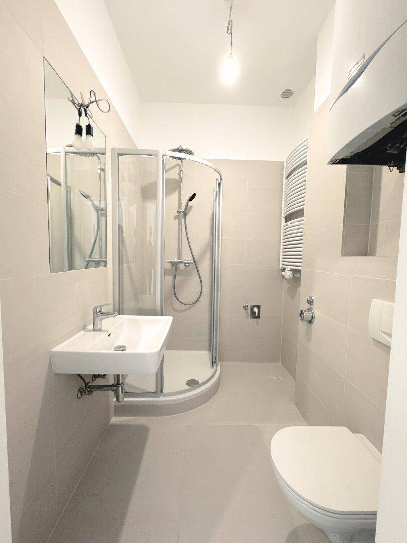 Modernes Badezimmer mit Duschkabine, Wand-WC und beheiztem Handtuchhalter in hellen Fliesen.