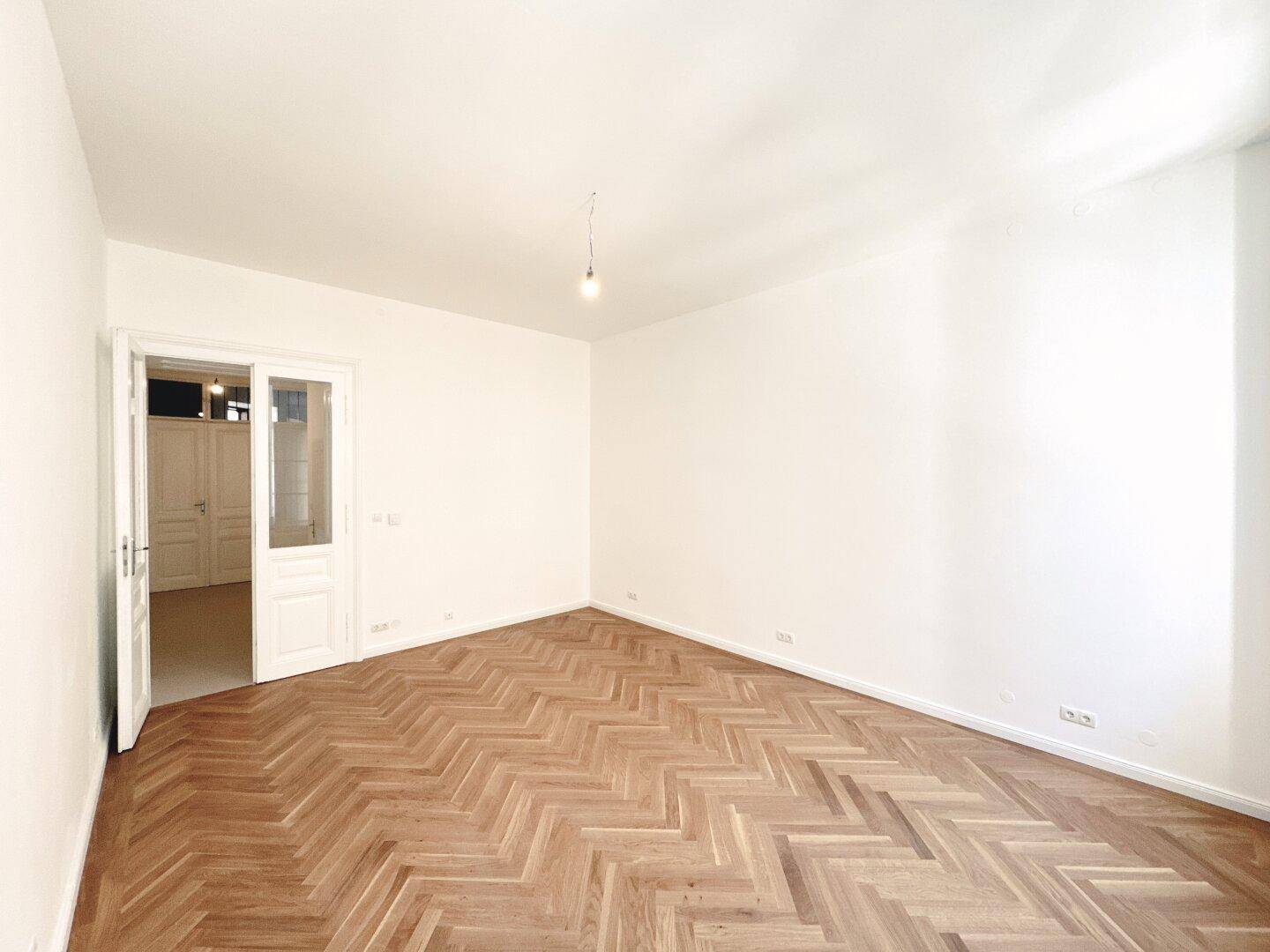 Helles Wohnzimmer mit Fischgrätparkett und hohen Decken, bereit für individuelle Gestaltung.