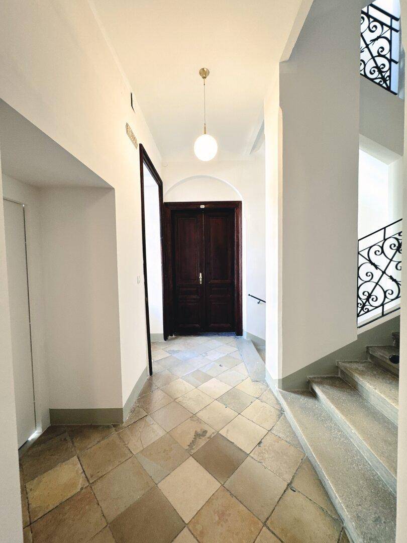 Heller Flur mit gemusterten Fliesen und einer eleganten Treppe mit schmiedeeisernem Geländer.
