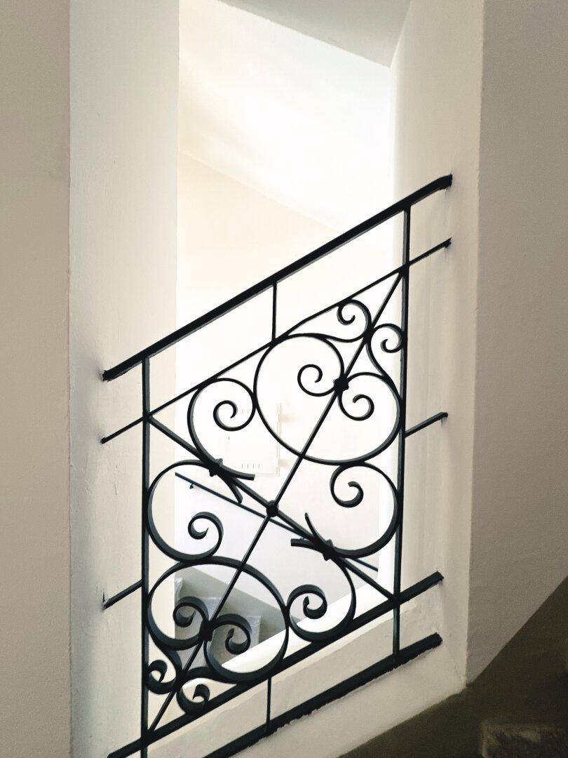 Detailansicht eines kunstvollen schmiedeeisernen Treppengeländers in einem historischen Gebäude.