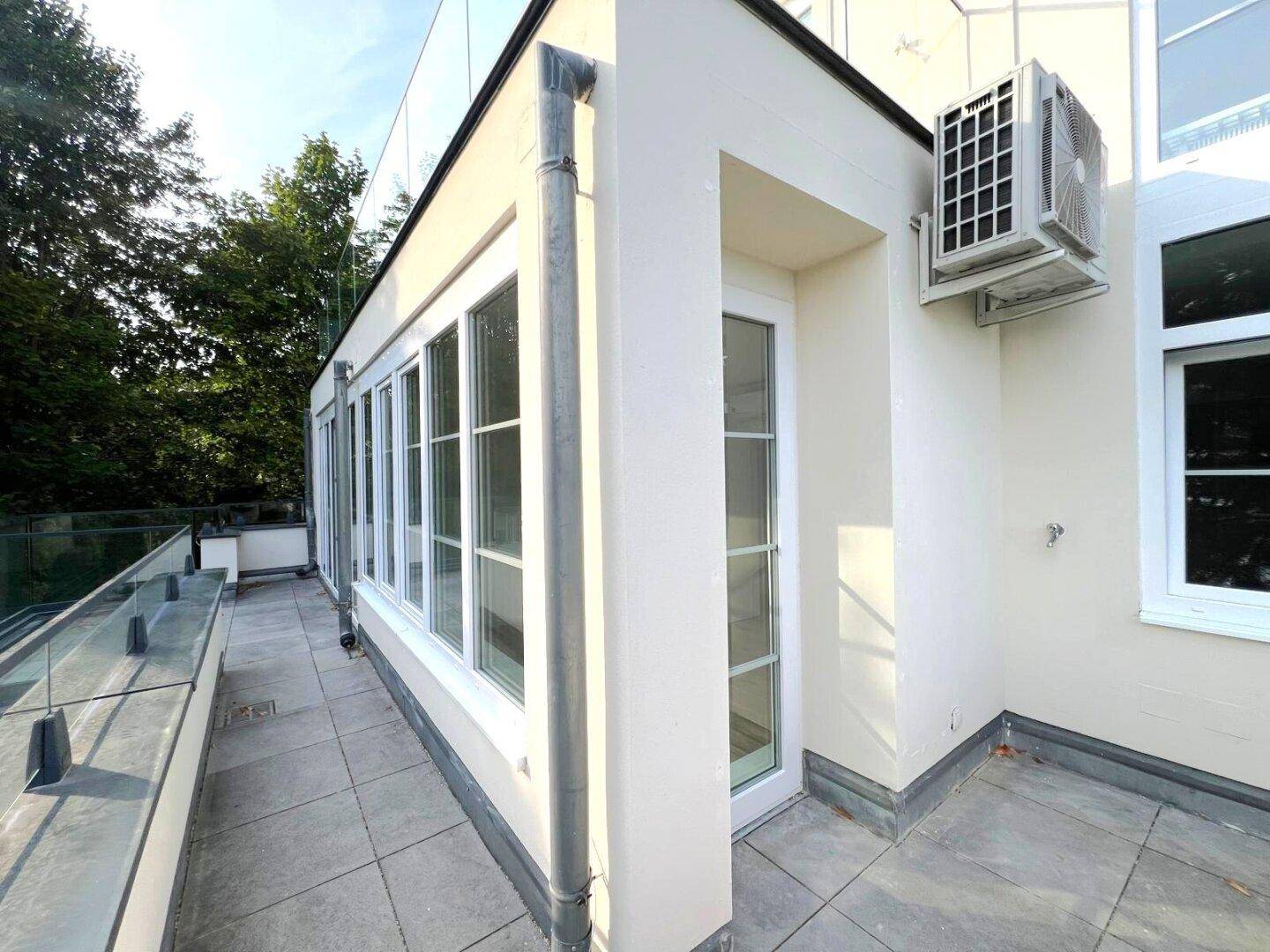 Ecke der Dachterrasse mit Klimaanlage an der modernen Fassade und Glasgeländer.