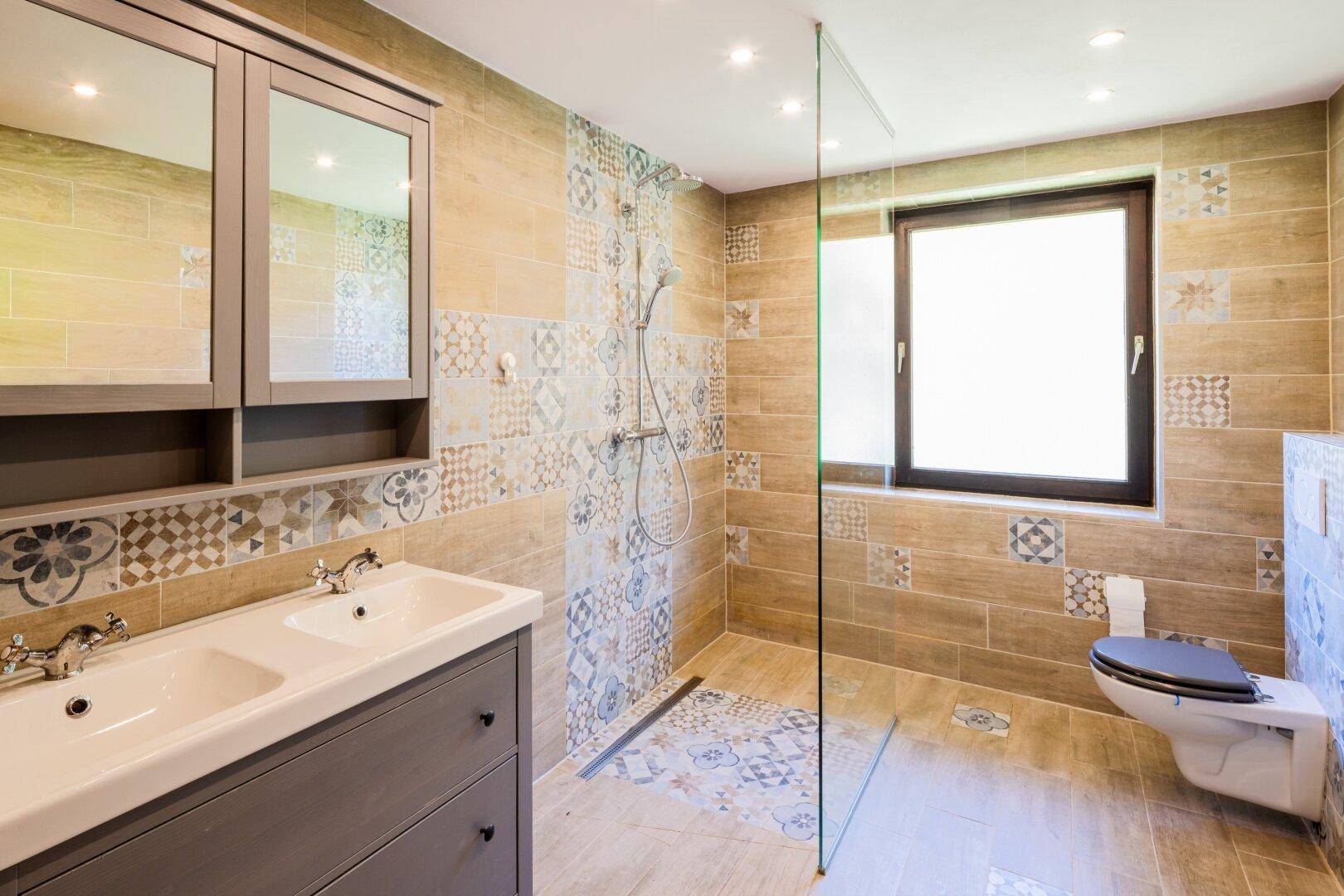 Modernes Badezimmer mit Doppelwaschbecken, begehbarer Dusche und gemusterten Fliesen.