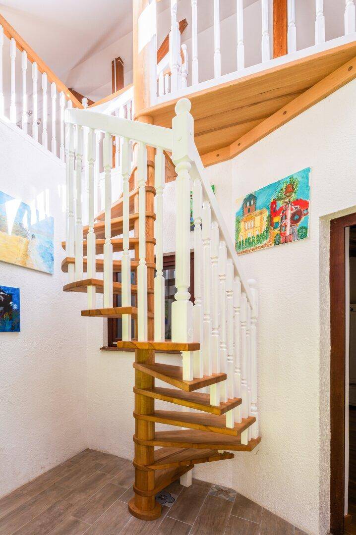 Elegante Holzwendeltreppe mit weißem Geländer, die verschiedene Ebenen verbindet.