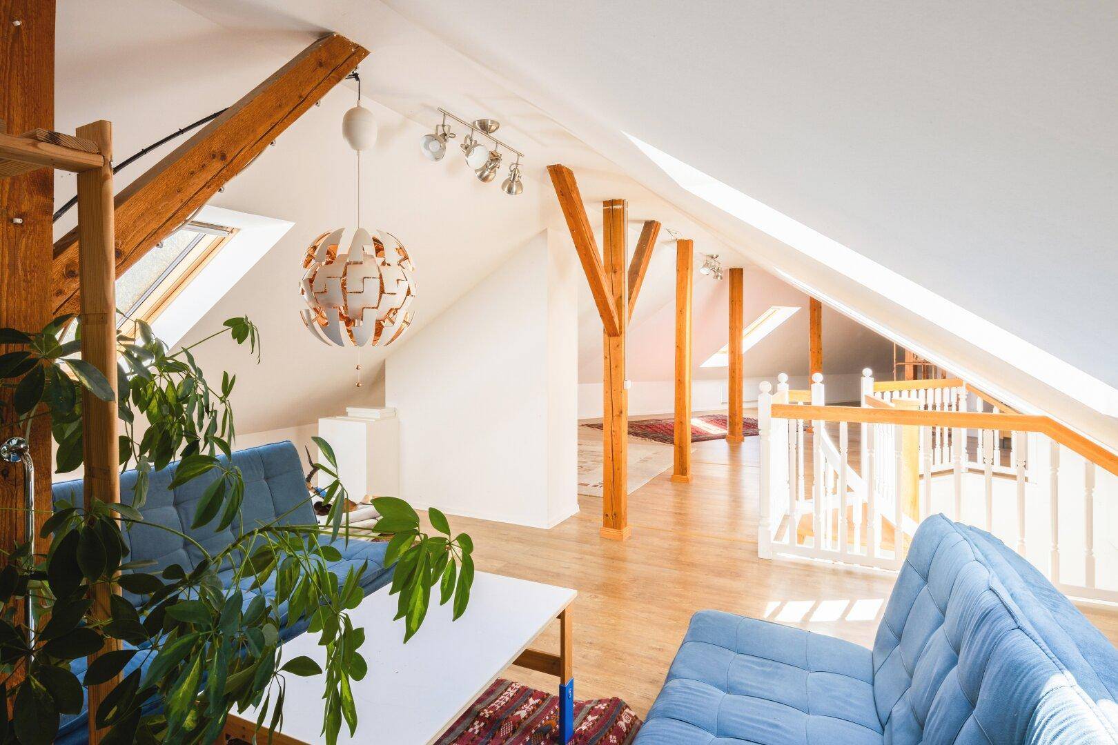 Helles Dachgeschoss mit Holzbalken, Dachfenstern und gemütlichen blauen Sofas.