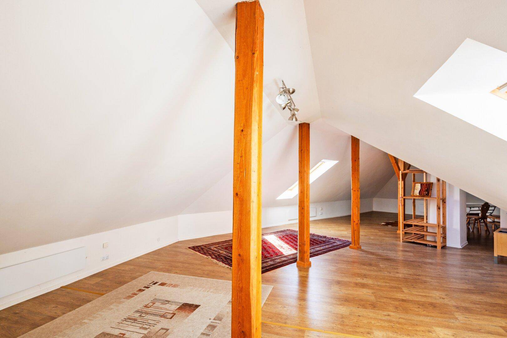 Weitläufiges Dachgeschoss mit sichtbaren Holzbalken und schrägen Wänden.