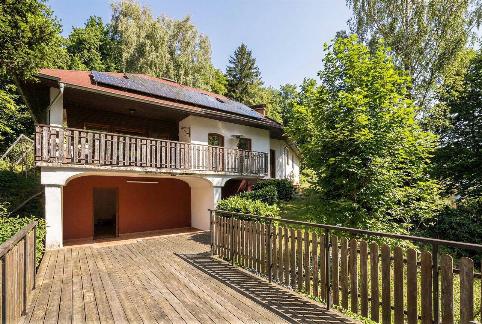 Rückansicht des Hauses mit großer Holzterrasse und Photovoltaikanlage auf dem Dach.