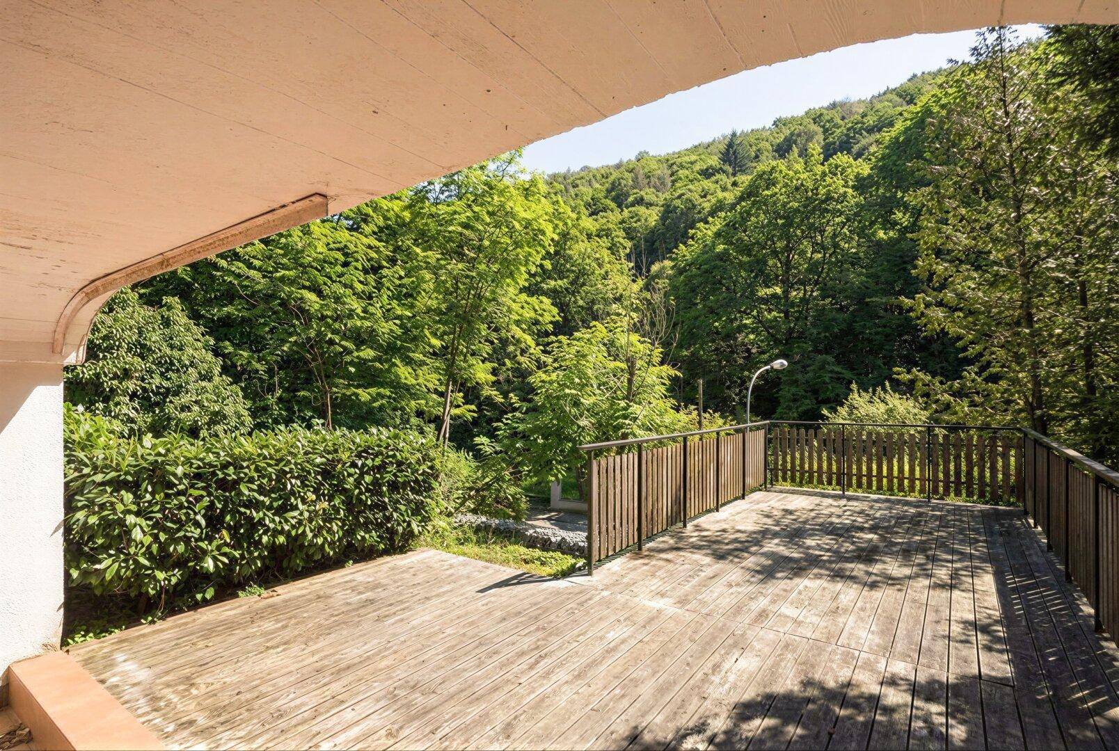 Geräumige Holzterrasse unter dem Balkon mit Blick ins Grüne und Hecke.