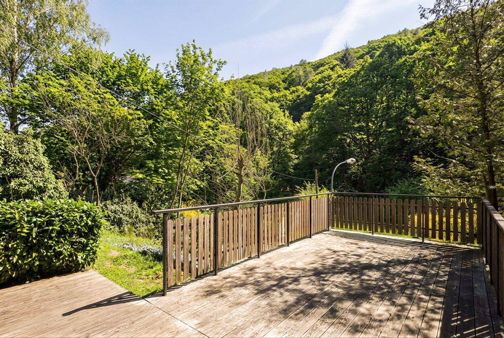 Weitläufige Holzterrasse mit Holzzaun und üppiger grüner Umgebung.