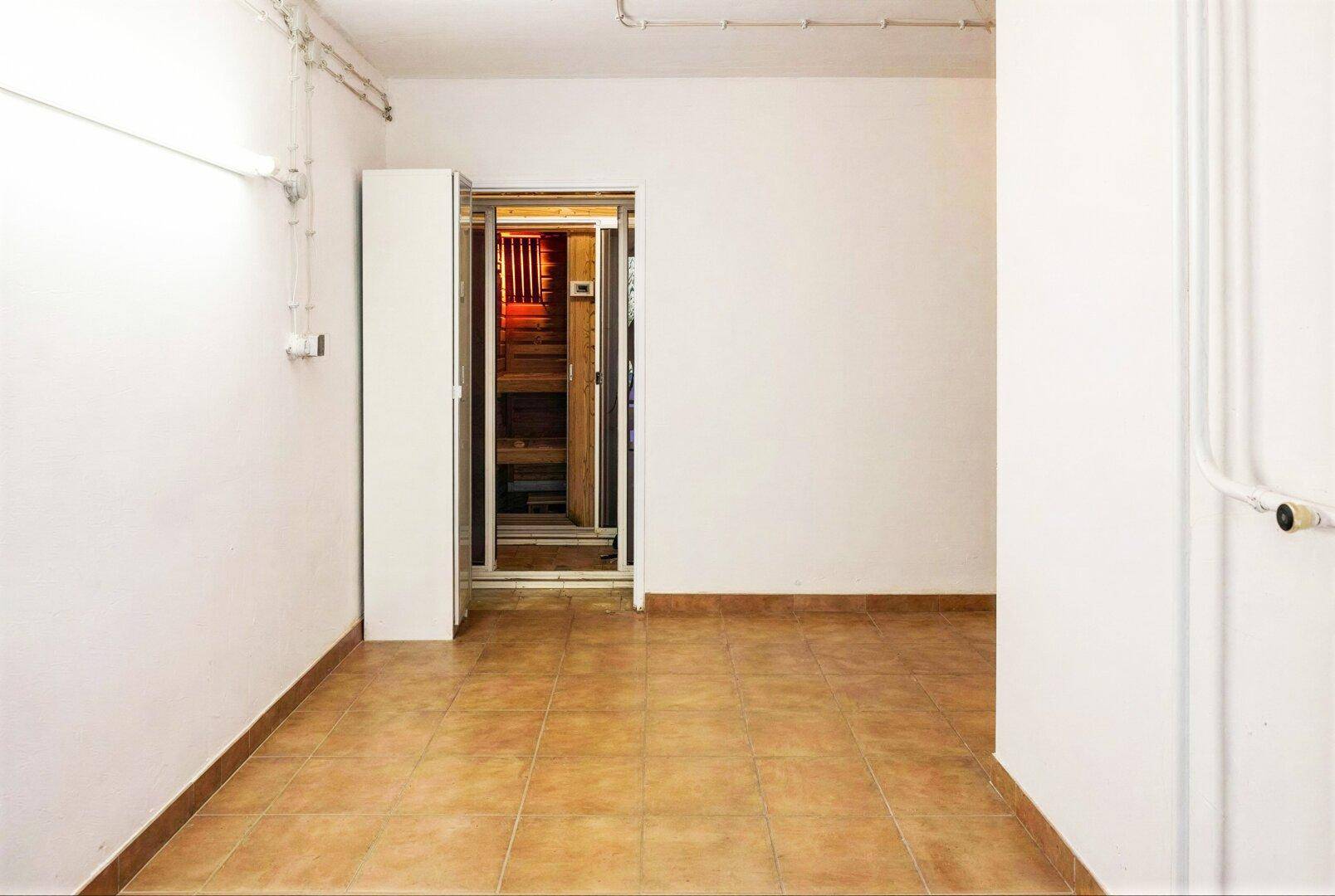 Heller Raum mit Fliesenboden und dem Eingang zu einer Sauna.