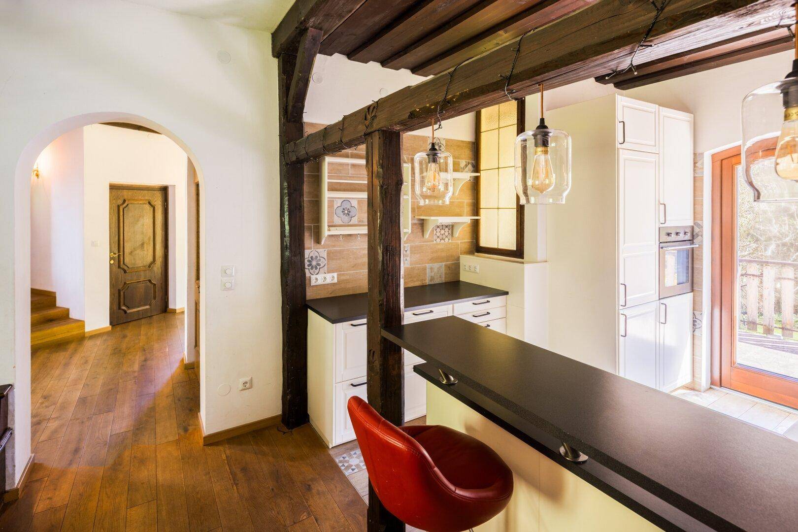 Moderne Küche mit Frühstücksbar, weißen Schränken und Holzbalken, offen zum Flur.