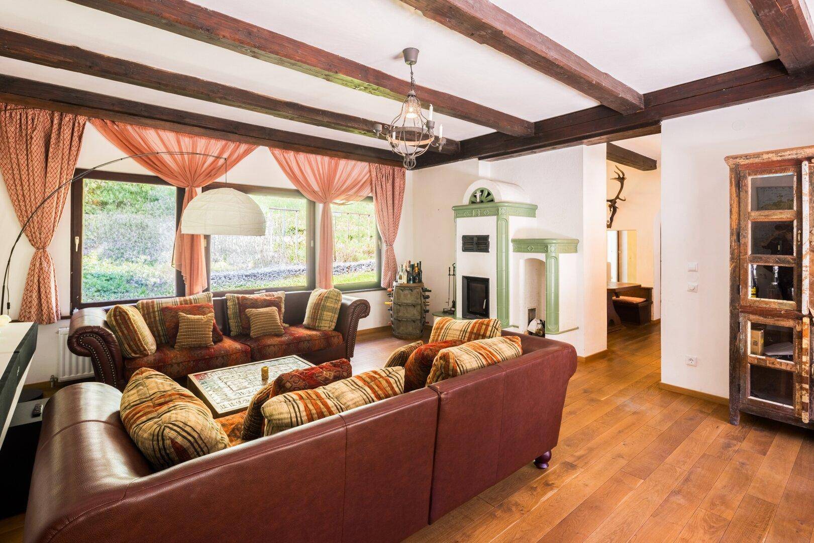 Gemütliches Wohnzimmer im Landhausstil mit Holzbalkendecke, Kachelofen und bequemen Sofas.
