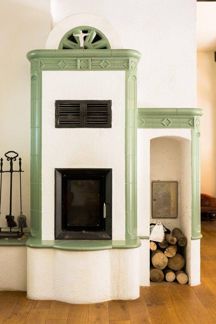 Nahaufnahme eines traditionellen grünen Kachelofens mit Holzscheiten im Wohnbereich.