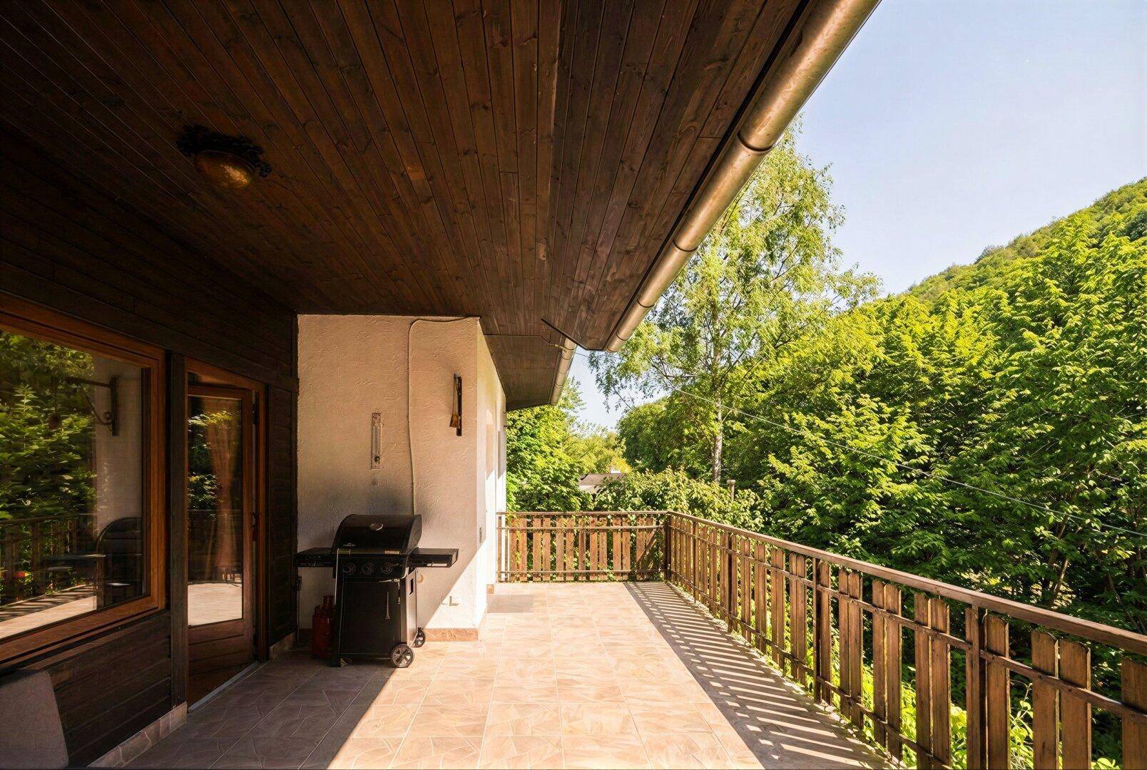 Langer Balkon mit Holzgeländer und Grill, bietet einen weiten Blick ins Grüne.