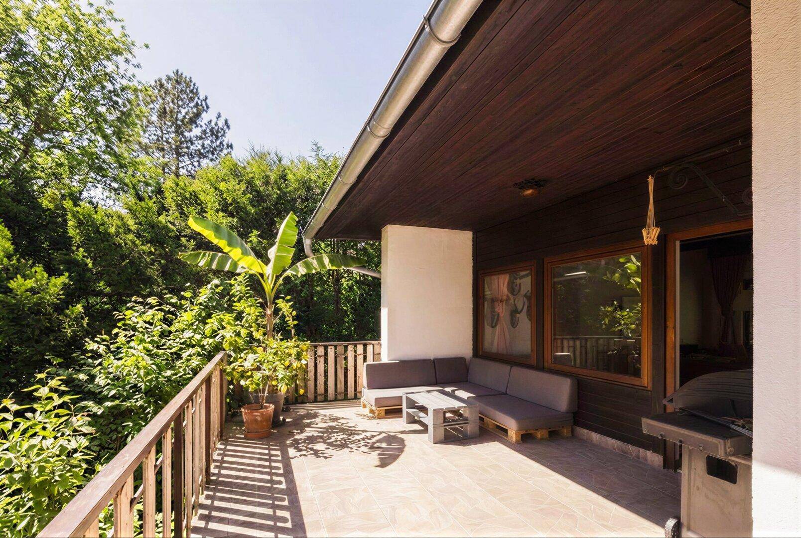 Geräumiger Balkon mit Outdoor-Sitzgruppe und Grill, umgeben von üppigem Grün.