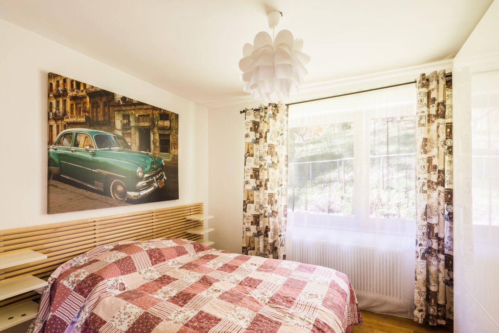 Gemütliches Schlafzimmer mit Doppelbett, farbenfroher Tagesdecke und Fensterblick.