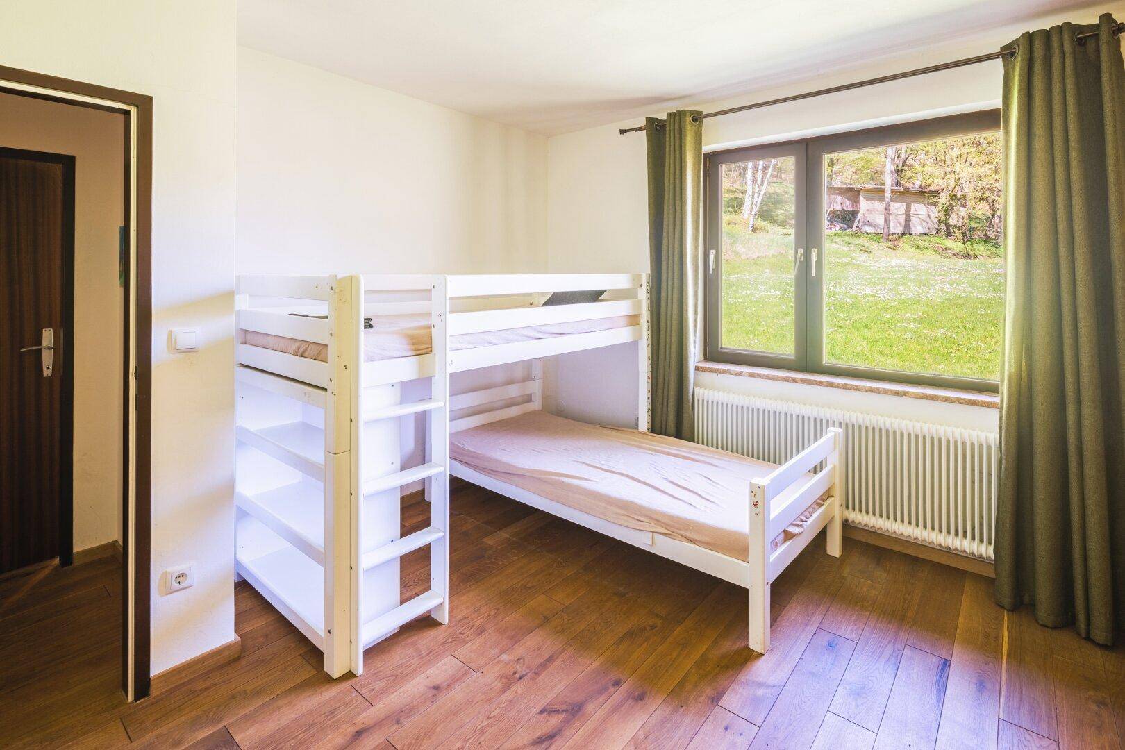 Kinderzimmer mit weißem Etagenbett und Blick ins Grüne durch das Fenster.