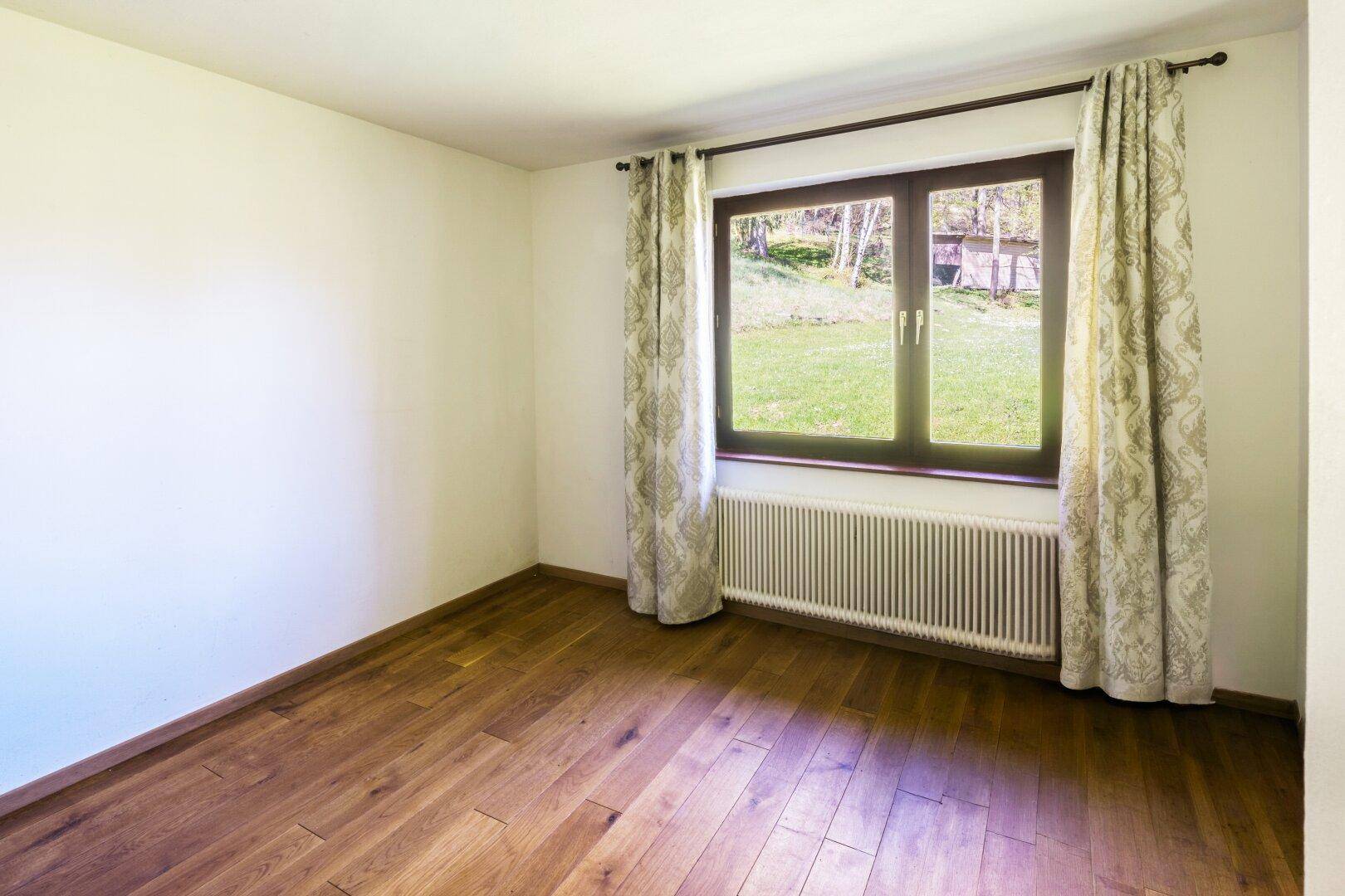 Helles, unmöbliertes Zimmer mit Holzparkett und Fenster mit Blick auf die Natur.
