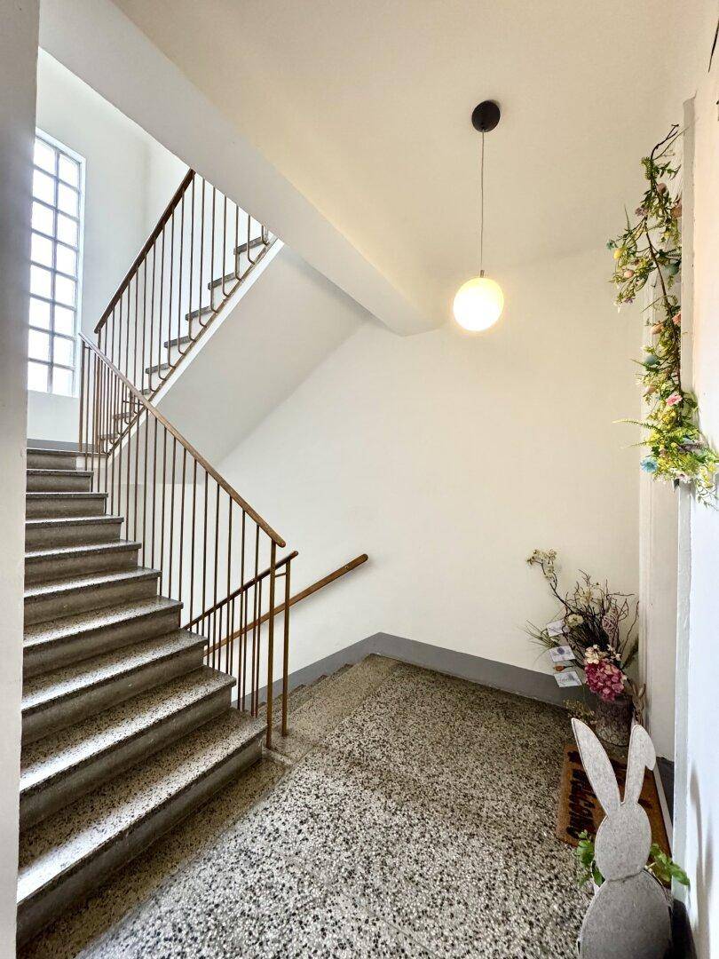 Treppenhaus mit Terrazzoboden, Metallgeländer und natürlichem Lichteinfall.