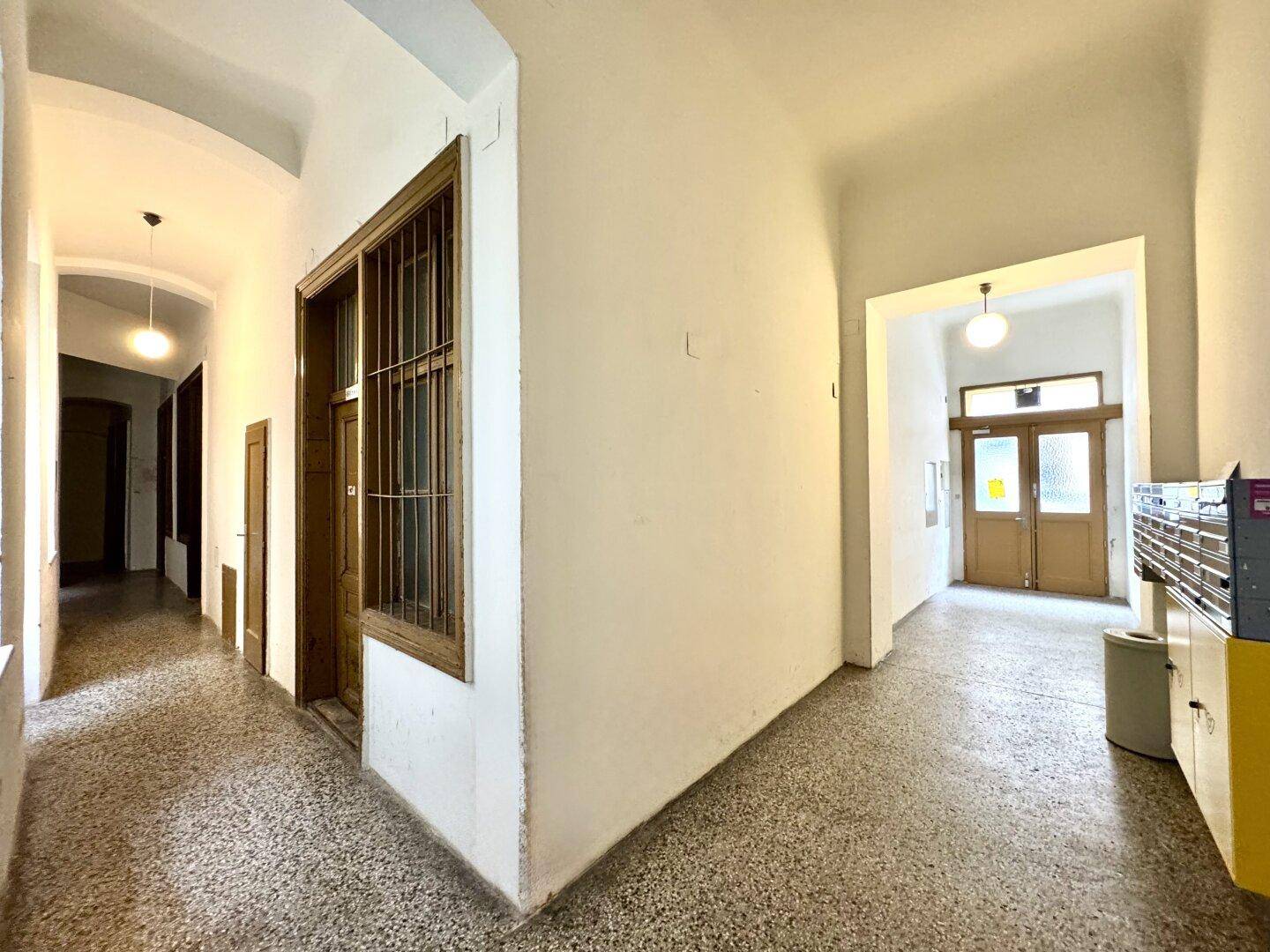 Gemeinschaftlicher Flur im Altbau mit Terrazzoboden und Holzfenstern.