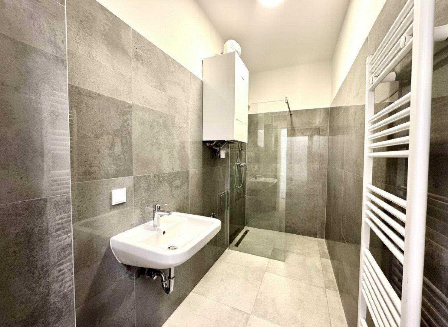Modernes Badezimmer mit grauen Fliesen, ebenerdiger Dusche und Waschbecken.