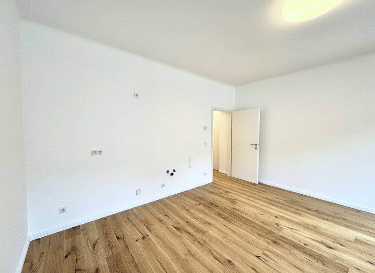 Leerer Raum mit Parkettboden und vorbereiteten Anschlüssen an der Wand.