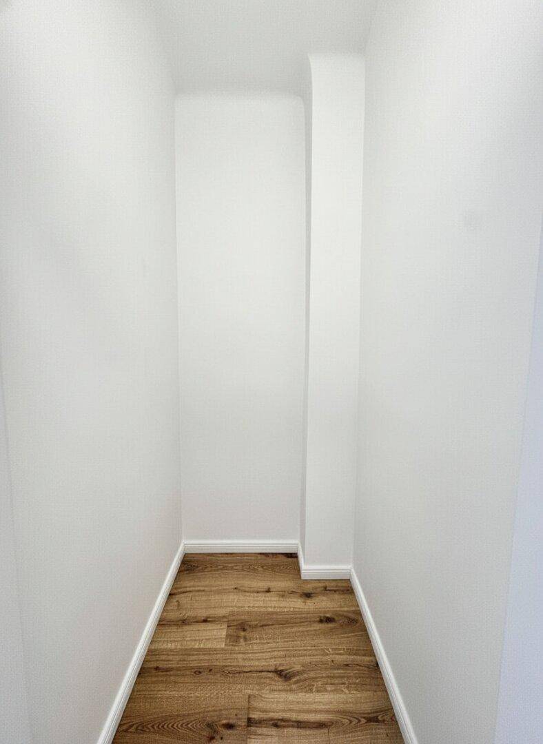 Kleiner Abstellraum oder begehbarer Schrank mit Parkettboden und weißen Wänden.