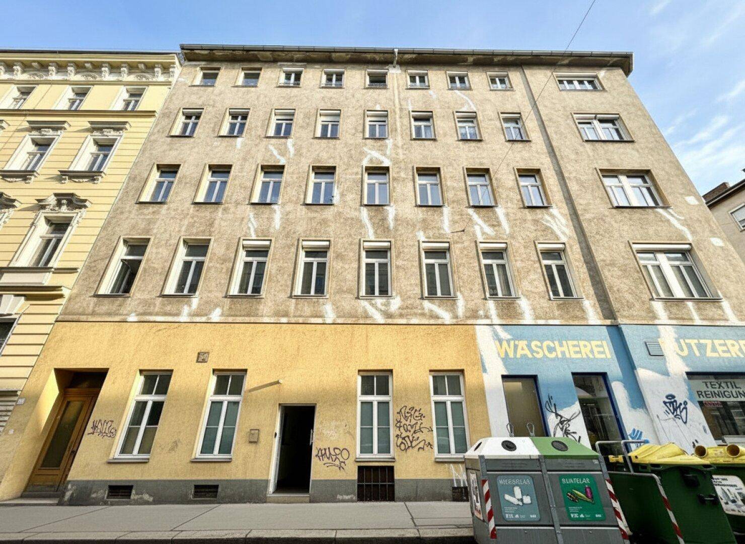 Fassade eines Mehrfamilienhauses mit Geschäften im Erdgeschoss und vielen Fenstern.