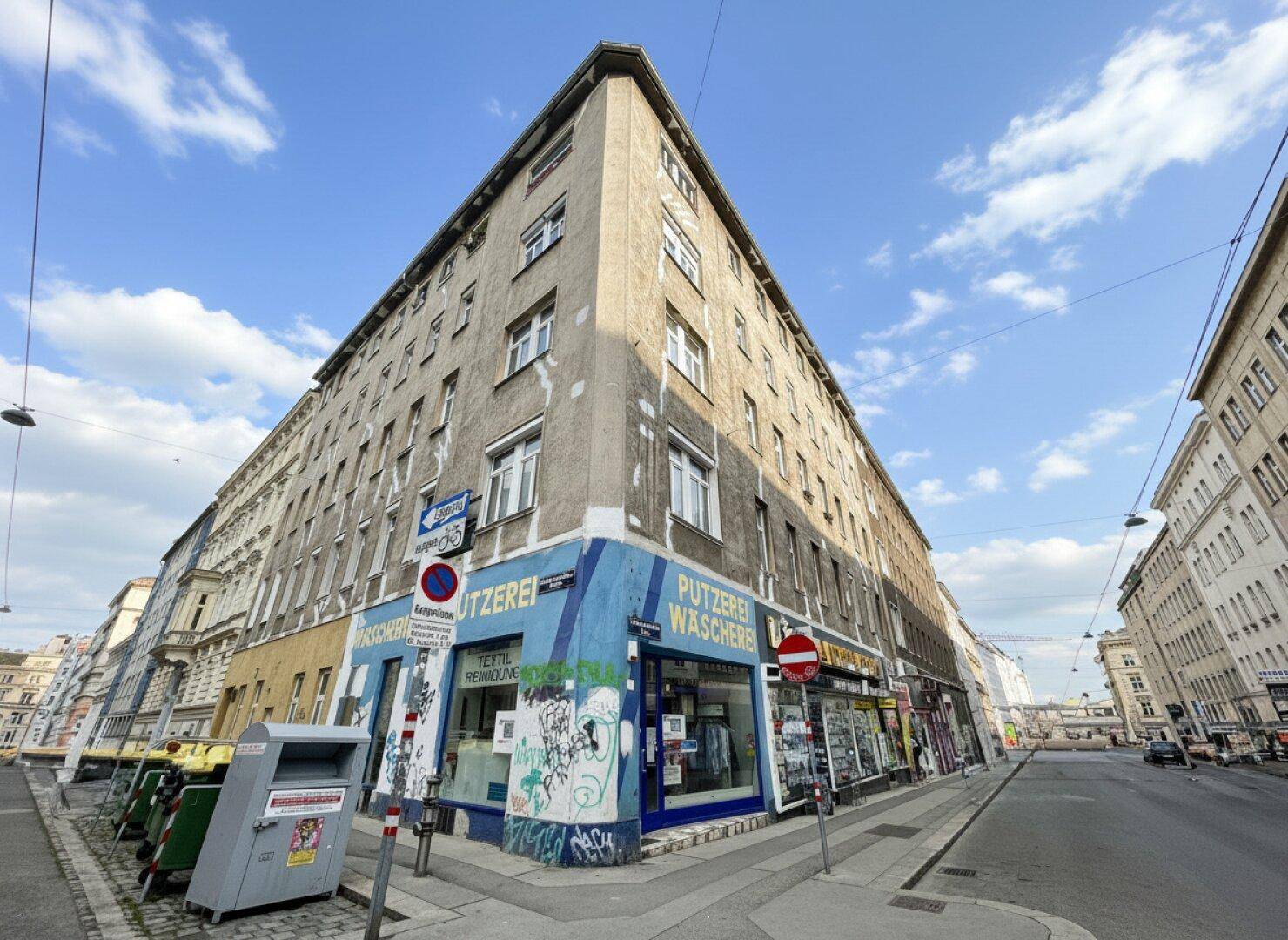 Eckgebäude in urbaner Umgebung mit Geschäften im Erdgeschoss und Wohnungen darüber.