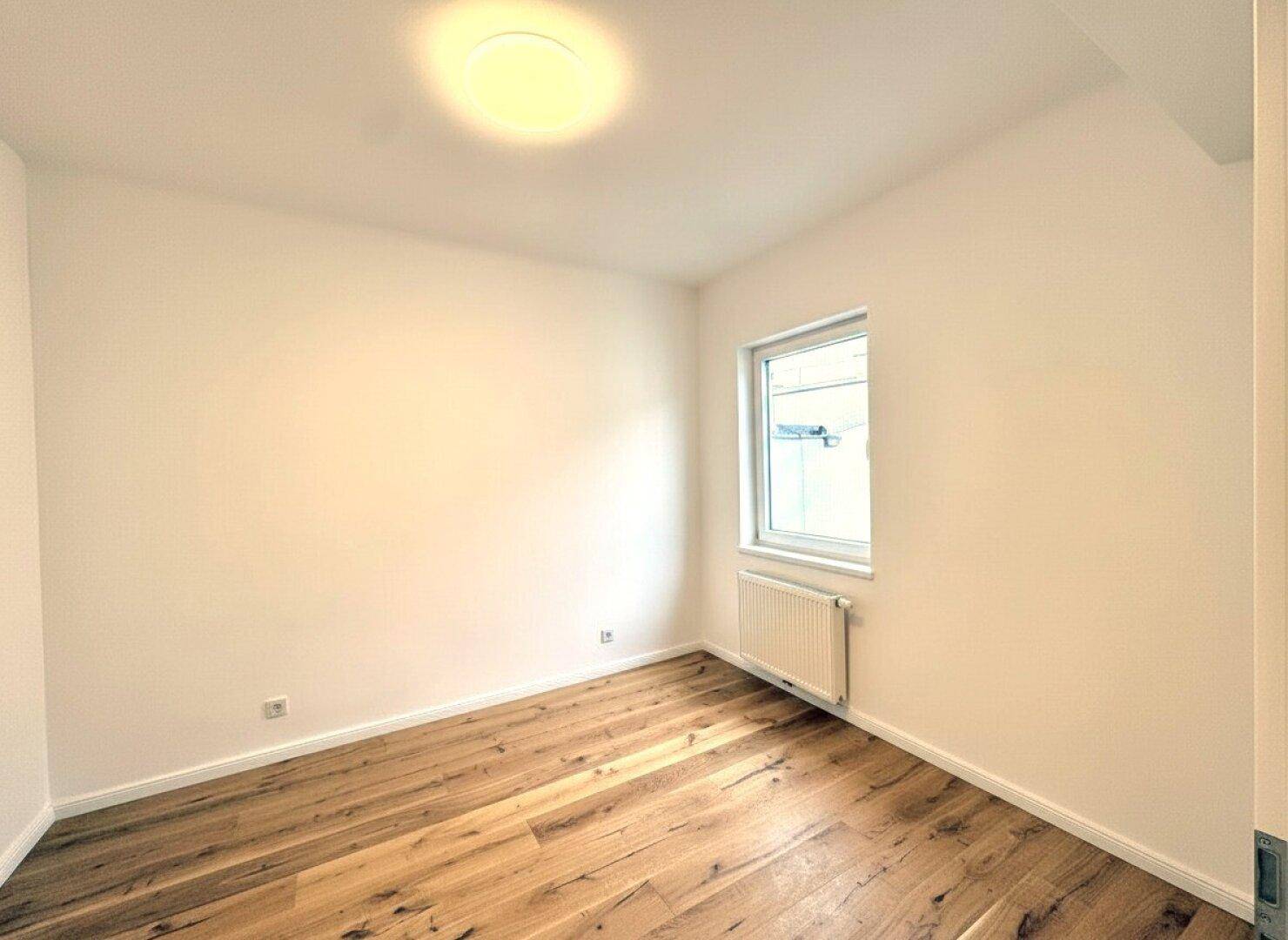 Heller, leerer Raum mit Parkettboden und einem Fenster, ideal für ein Kinderzimmer.