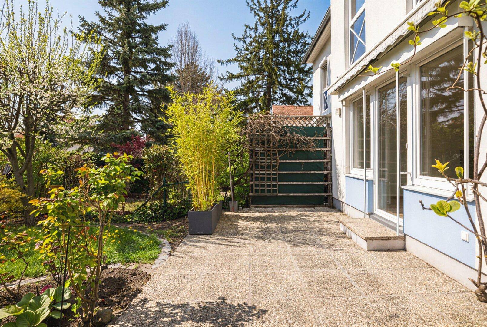 Sonniger Terrassenbereich mit Steinplatten und Zugang zum grünen Garten des Hauses.