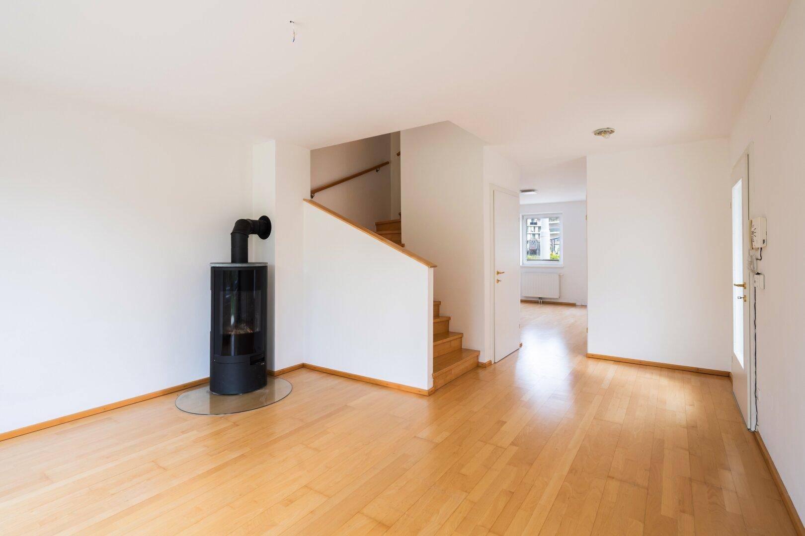 Geräumiger Wohnbereich mit Holzfußboden, modernem Kaminofen und Treppenaufgang.