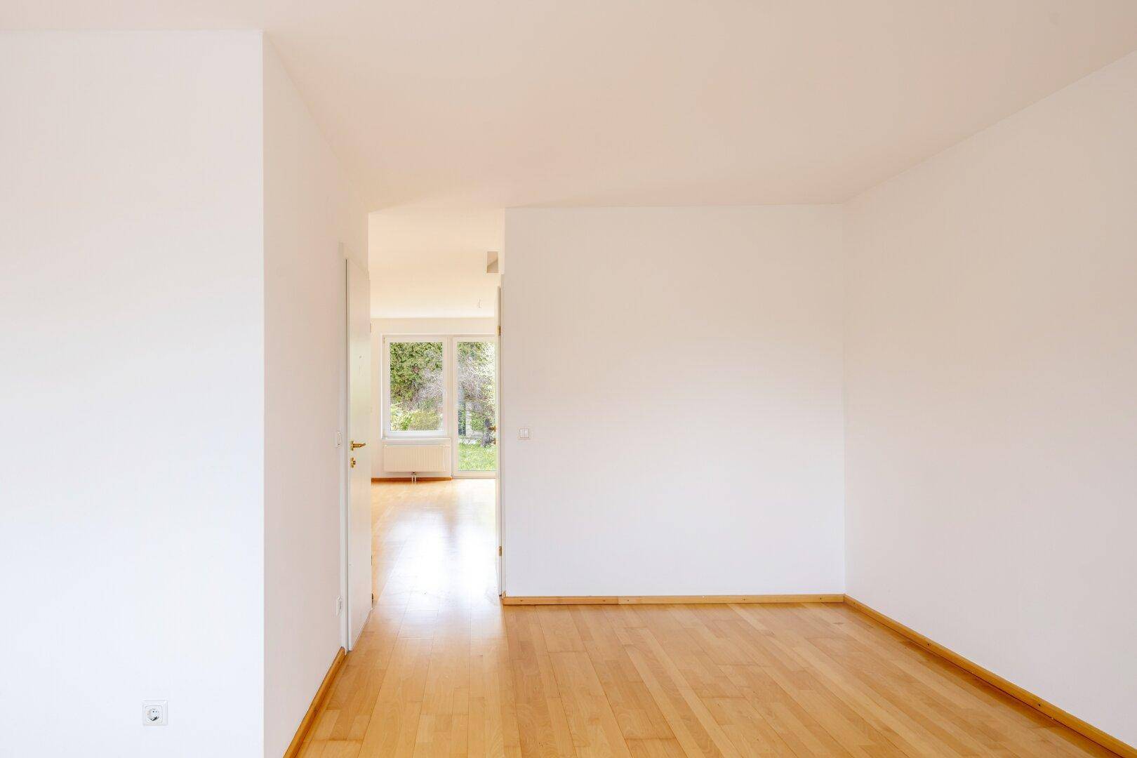 Leerer Raum mit hellem Holzfußboden und Blick auf den grünen Außenbereich.