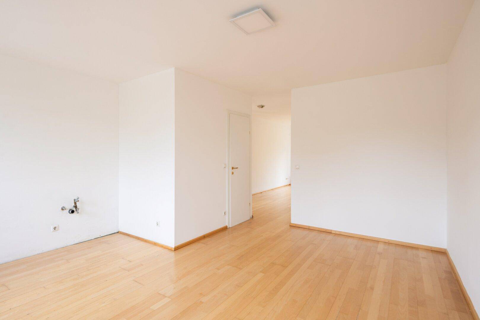 Leerer Küchenbereich mit Anschlüssen für Geräte und hellem Holzfußboden.