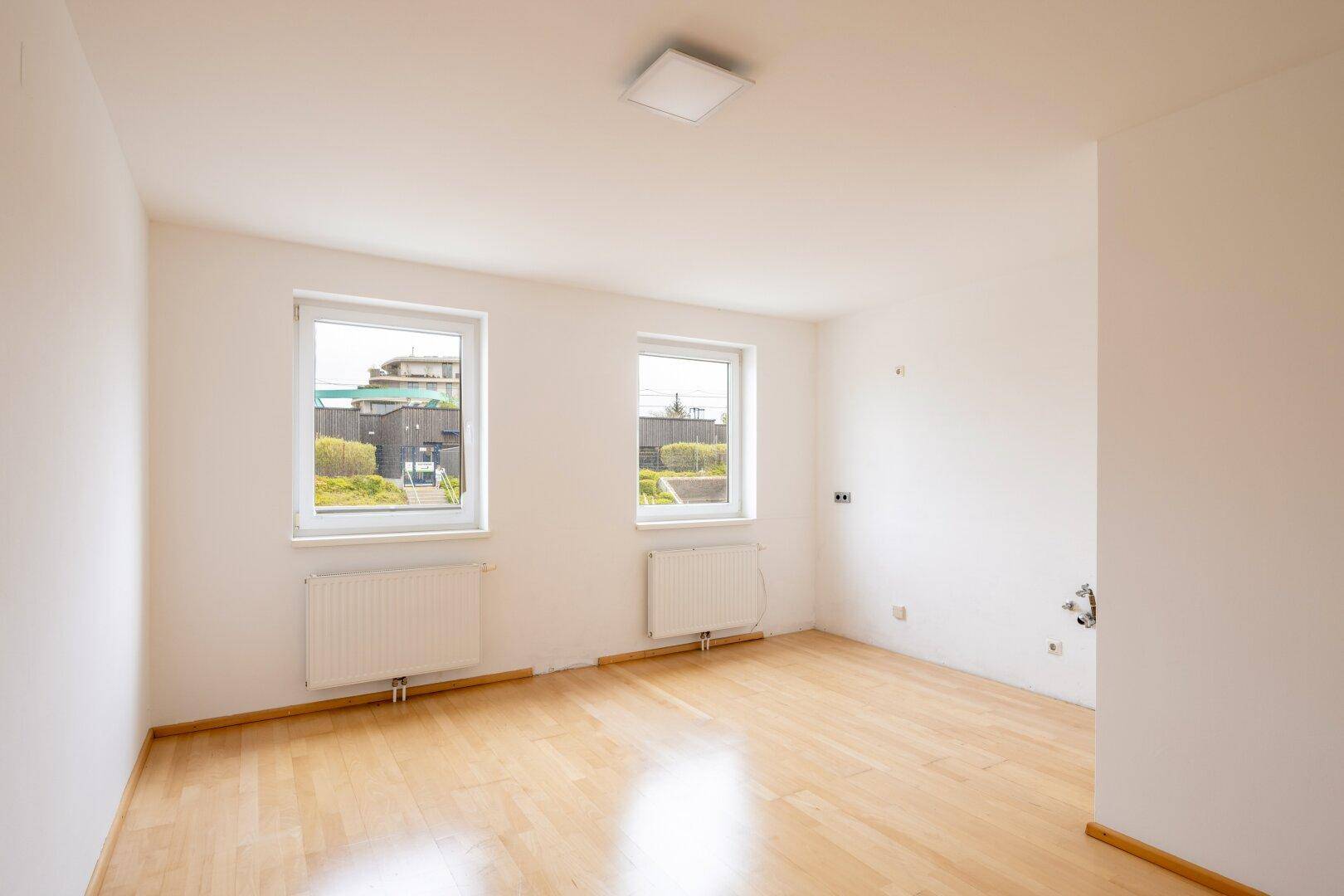 Helles, leeres Zimmer mit Holzfußboden und zwei Fenstern, bereit zur individuellen Gestaltung.
