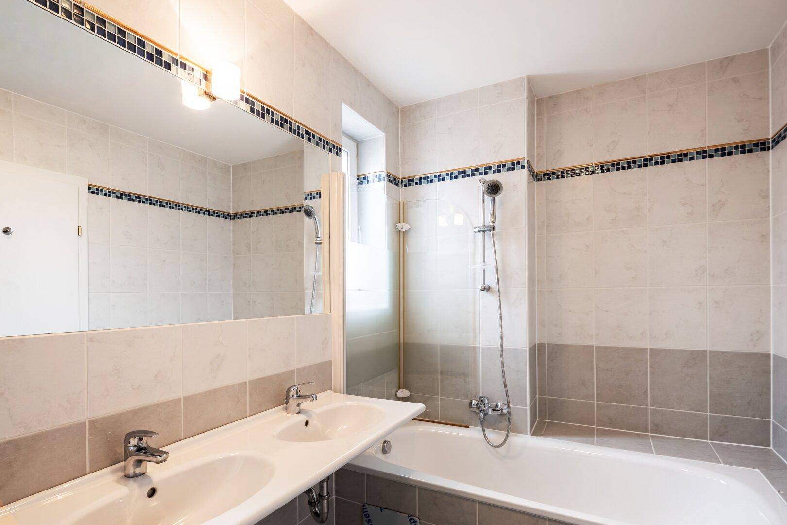 Gefliestes Badezimmer mit Doppelwaschbecken, Badewanne und Spiegel.