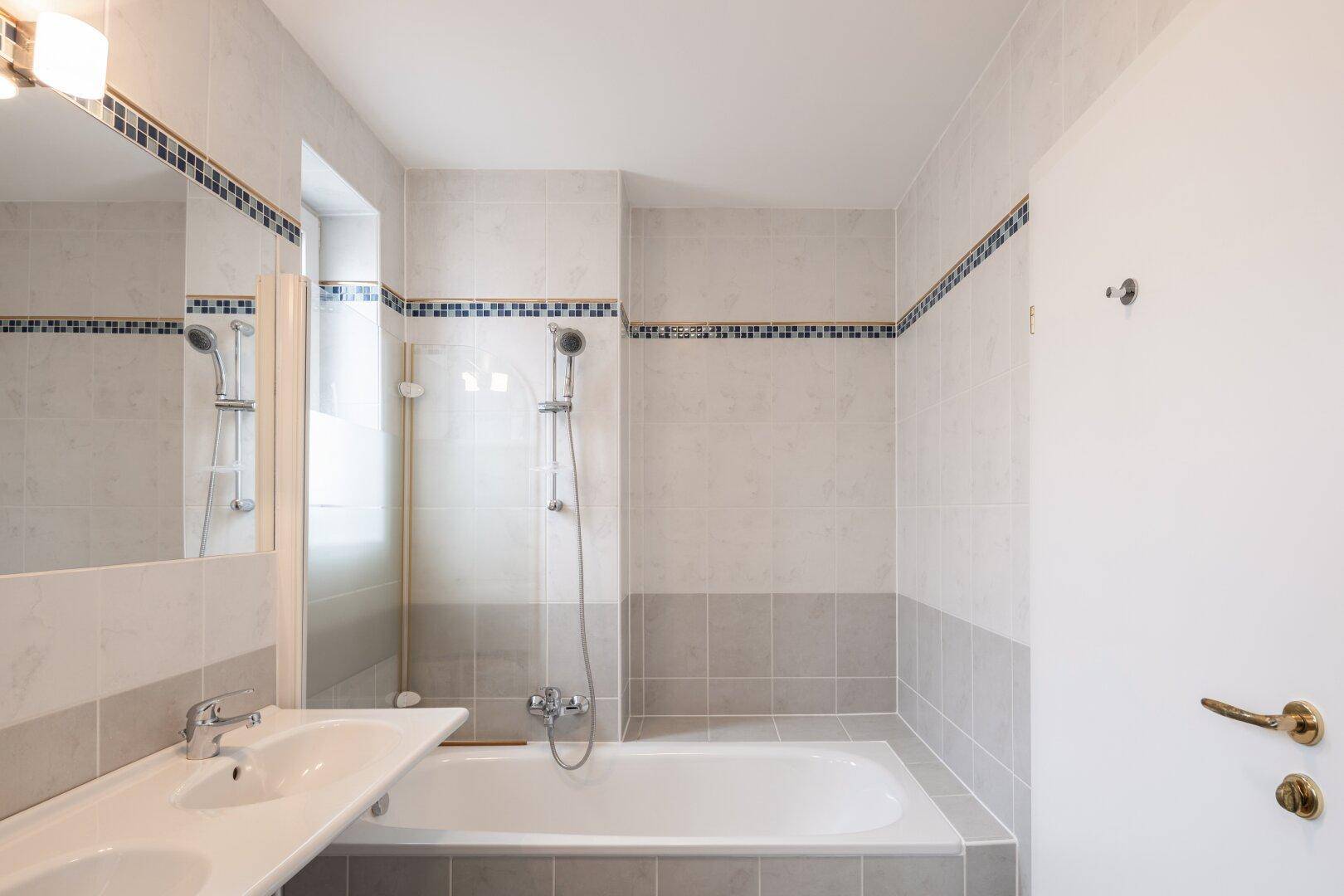 Modern gefliestes Badezimmer mit Badewanne, Doppelwaschbecken und Duschvorrichtung.