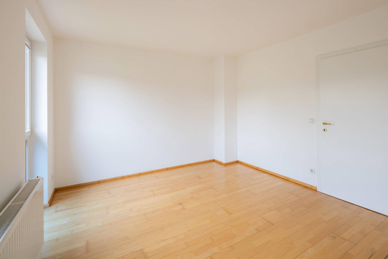 Leerer Raum mit hellem Holzfußboden und einem Fenster, bereit zur Einrichtung.